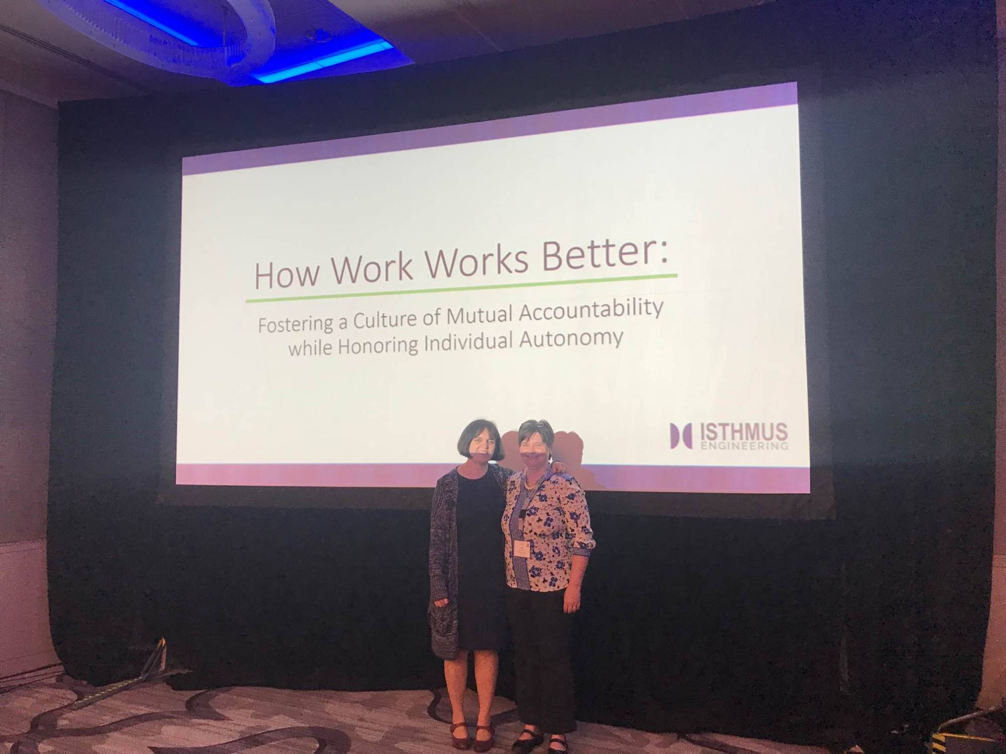Katie and Mary standing in front of presentation title slide that says How Work Works Better: Fostering a Culture of Mutual Accountability while Honoring Individual Autonomy