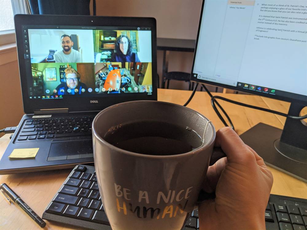 A hand holding a mug of tea in front of a laptop screen with a Zoom meeting grid of faces
