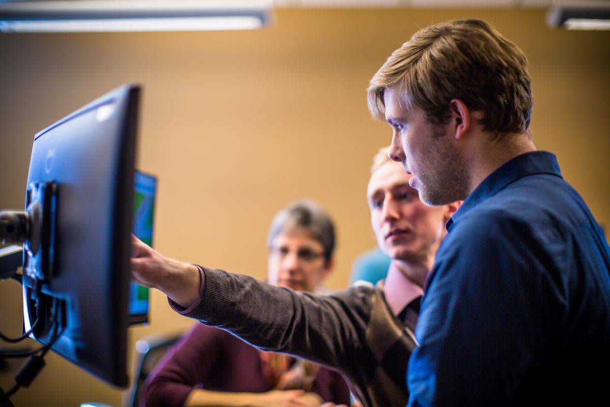 Three people standing and looking at a computer monitor